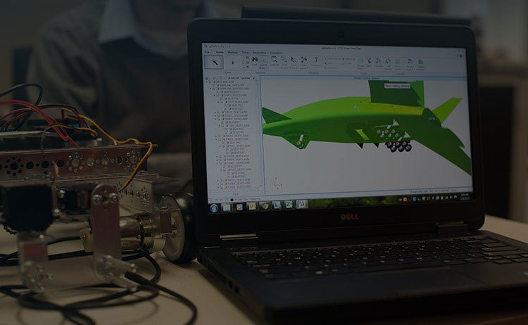 Ordinateur portable affichant une pièce modélisée dans un logiciel de CAO de PTC, à côté d’un prototype électronique.
