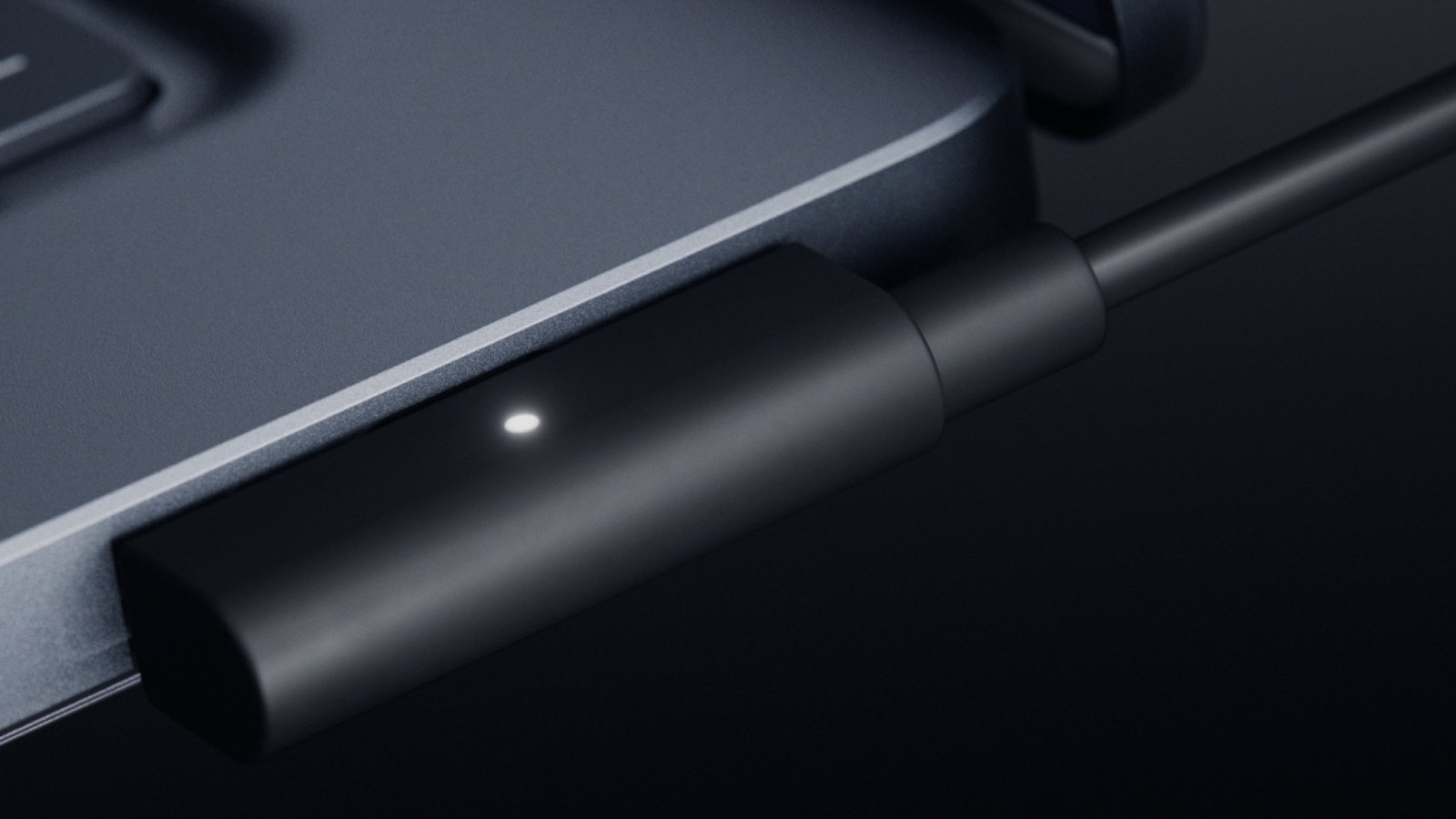 Gros plan sur le connecteur USB-C magnétique noir branché sur le flanc du Surface Laptop Ultra, avec un témoin lumineux blanc.